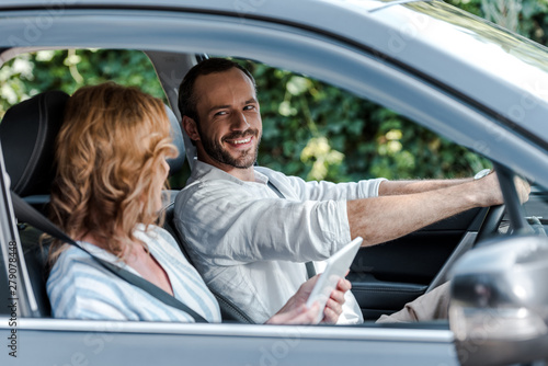 selective focus of happy man driving car and looking at woman with digital tablet © LIGHTFIELD STUDIOS