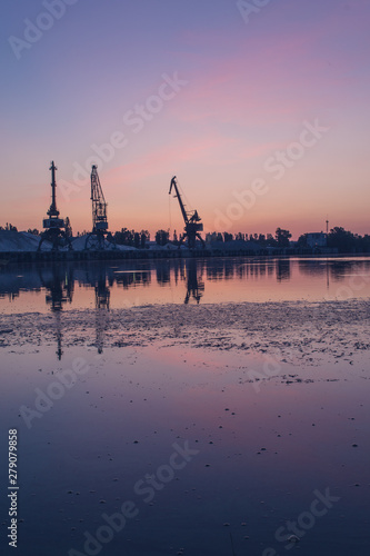 Sunrise over the port. Dawn over the river. The cranes in the industrial part of the city on the shore.