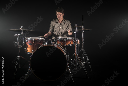 Professional drummer playing on drum set on stage on the black background