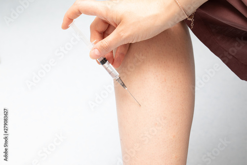 A young Caucasian woman is viewed closeup, inserting a hypodermic needle into her leg. Rapid delivery of drugs into the body to treat ailments such as diabetes.