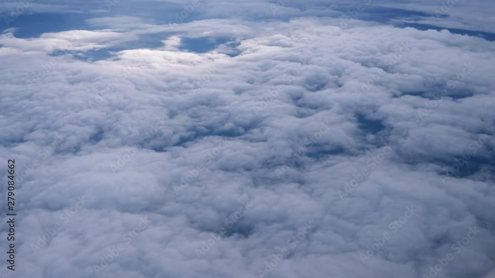 Aerial view from the airplane. Flying over the layer of clouds and looking on landscape through the clouds. Soft sunlight in sky. Aerial view from the airplane. Flying over the layer of clouds and looking on landscape through the clouds. Soft sunlight in sky.