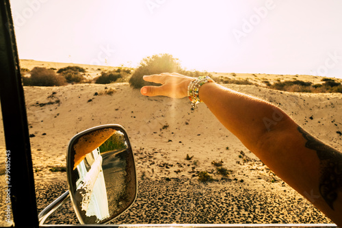 Travel and freedom concept for alternative lifestyle people - close up of hand of a caucasian woman outside the window of the vintage car playing with the wind while traveling - desert  and sunlight photo