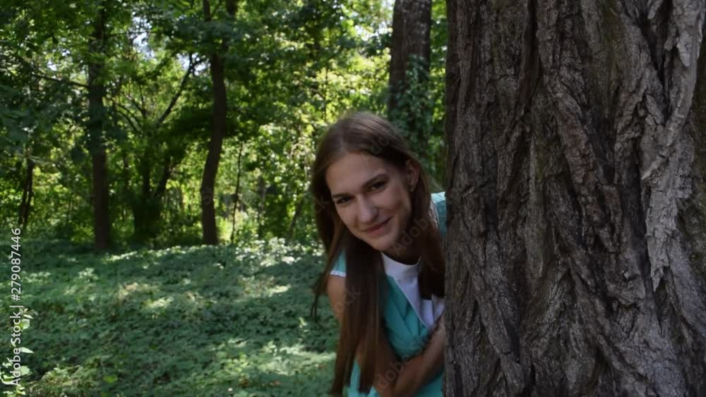 Young girl peeking from behind a tree in nature. Young girl peeking from behind a tree in nature.