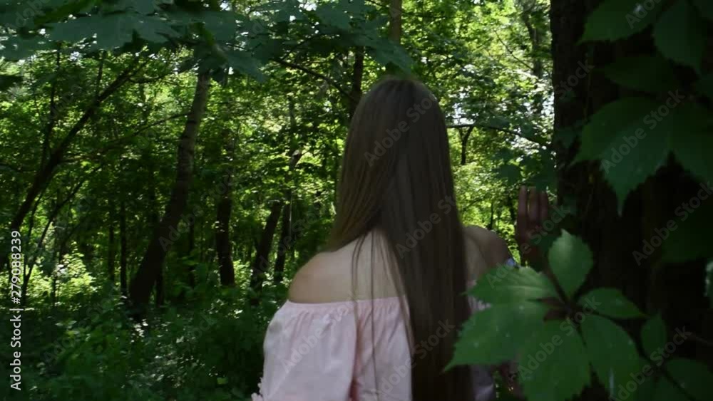 A young girl walks around a tree with green foliage. Forest. A young girl walks around a tree with green foliage. Forest.