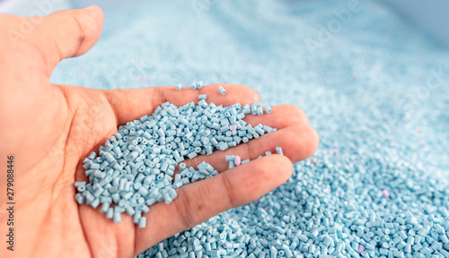 Hand on large pile of blue plastic granules in temporary storage of production line at recycle factory, masterbatch dye polymer plastics resin pellet background,  injection molding process lab