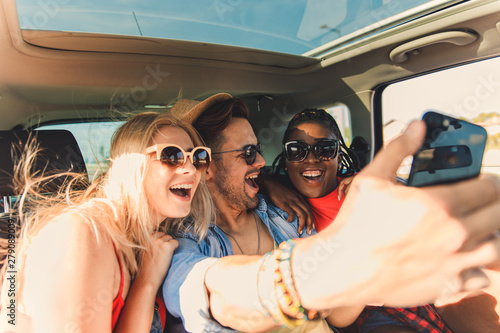 Three best friends enjoying traveling in the car, sitting in rear seat and having lots of fun making selfie on a road trip. © Zoran Zeremski