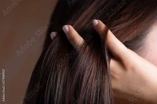 A close up view of a gorgeous young brunette lady with lacquered nails. Combing her fingers through the straight, sleek and conditioned hair. Copy space on the left.
