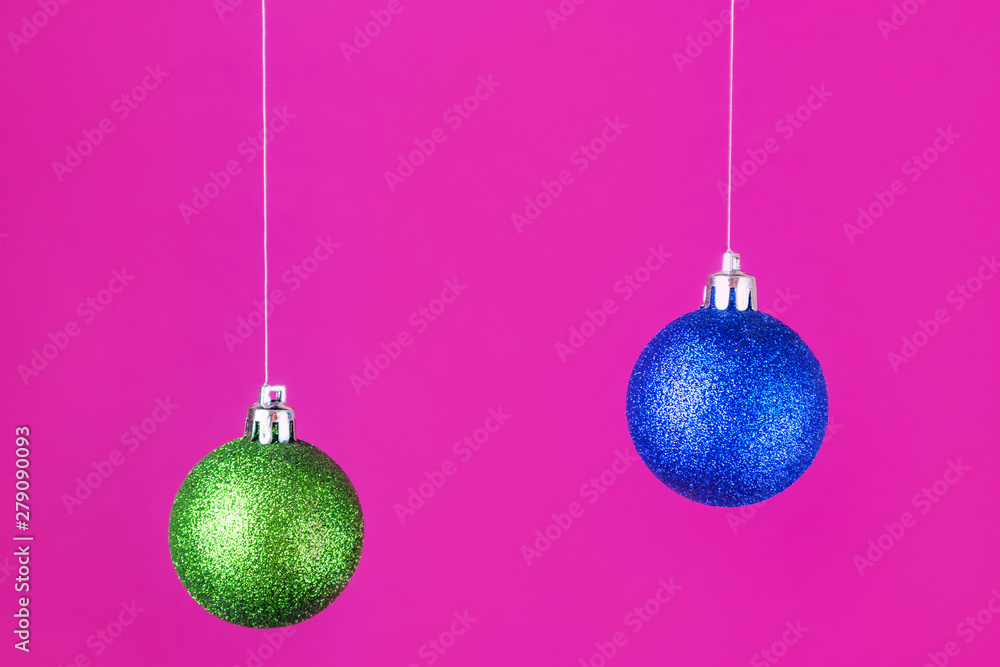 Obraz premium A bright New Year concept - blue and green Christmas balls hanging on a pink background. Place for text, minimalism.
