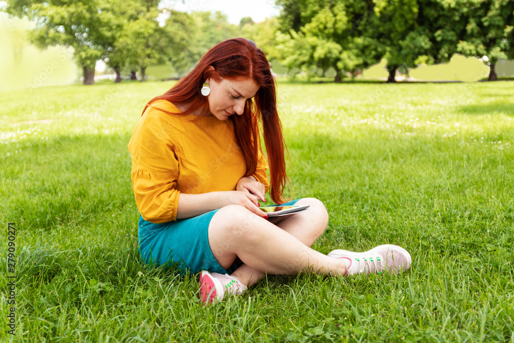 Beautiful young girl using a tablet at sunset, in the park. Relaxing concept