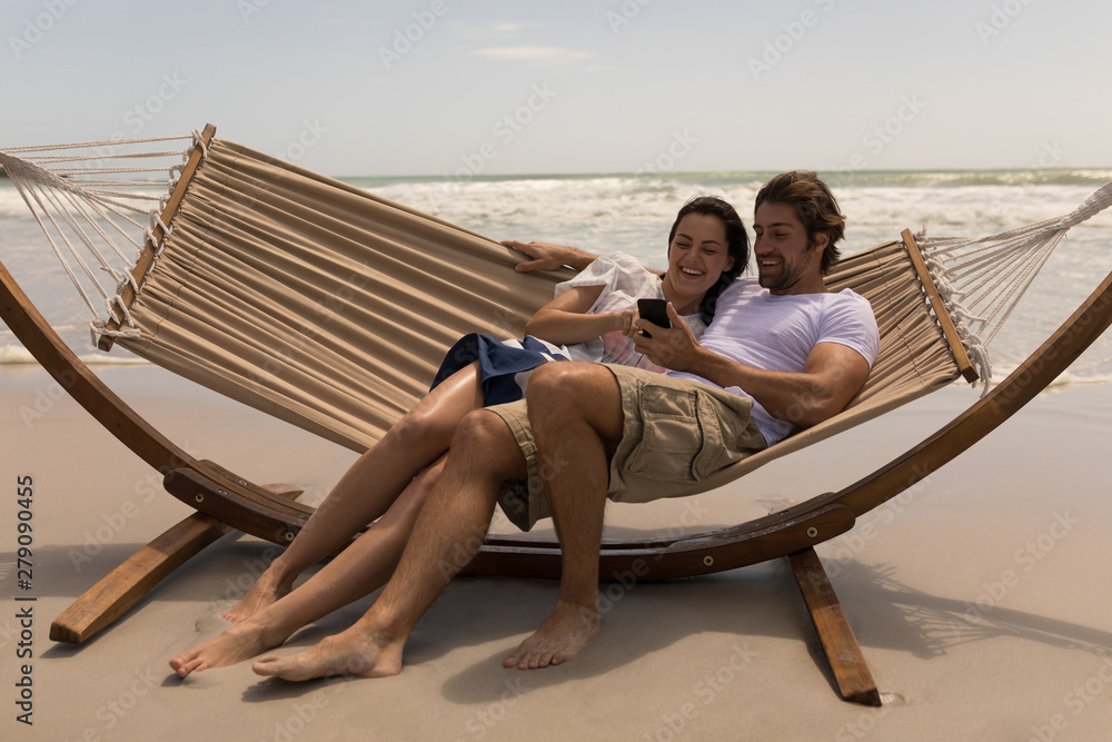 Couple relaxing on hammock and using mobile phone 