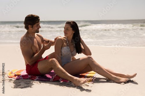 Man applying sunscreen lotion on woman back at beach