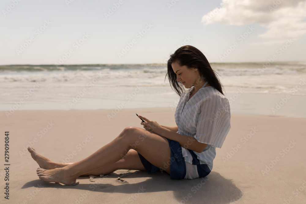 Beautiful young woman using mobile phone at beach