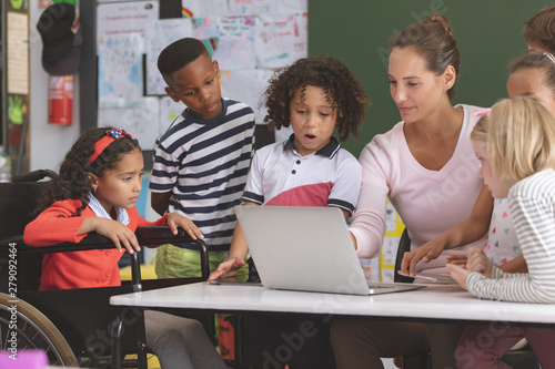 Teacher and school kids discussing over laptop in classroom photo