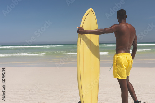 Male surfer with a surfboard standing on a beach on a sunny day