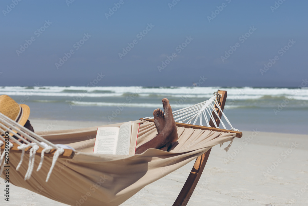 Man reading book while relaxing on hammock at beach