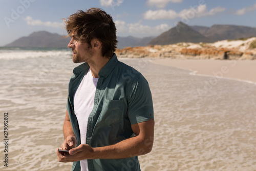 Young man looking away while using mobile phone on beach