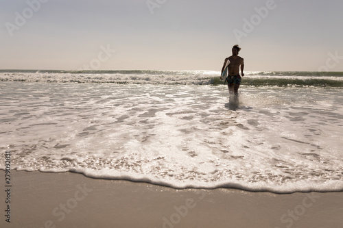 Young male surfer with surfboard running on beach