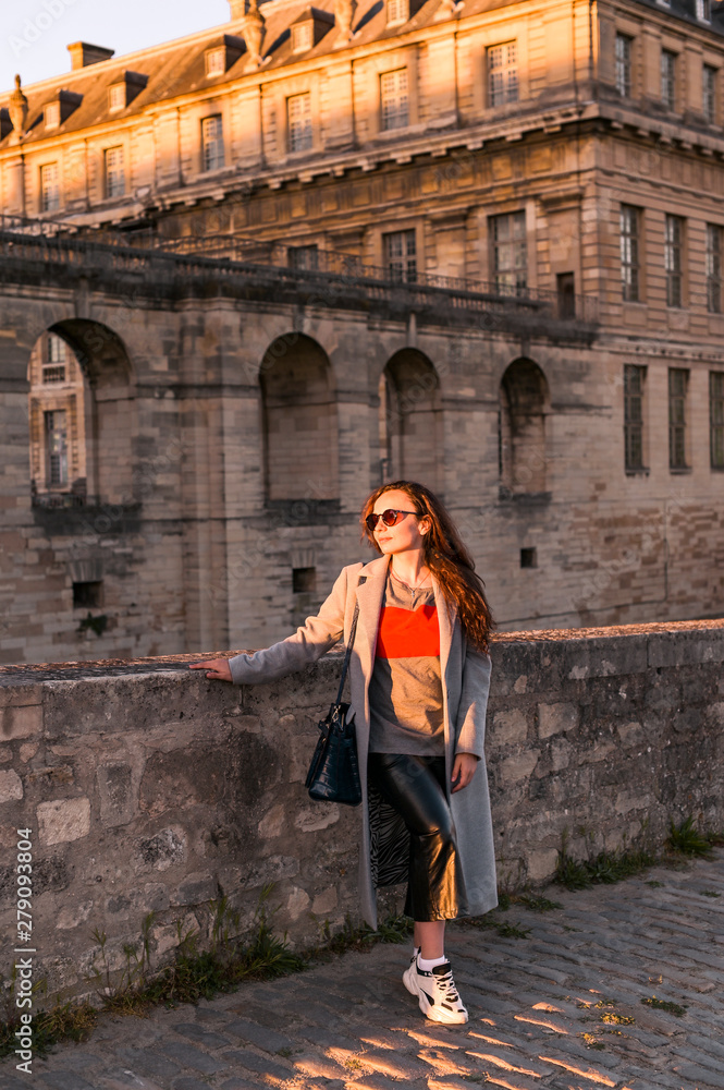The girl near the old castle in France. Vincennes Castle in the rays of the sun at sunset. Travel and tourism.