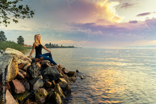 Beautiful young woman sits on the rocks by the Balaton lake photo