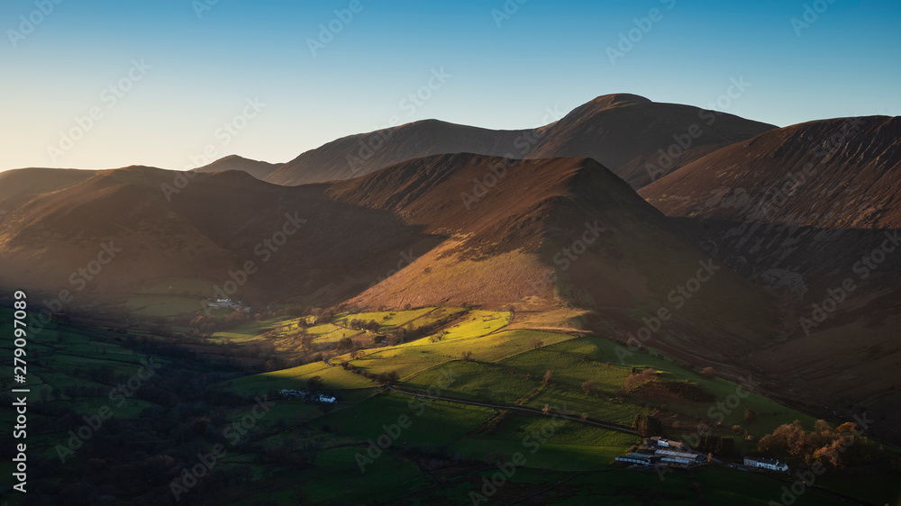 Beautiful Autumn Fall landscape image of sun beams lighting up small area of mountain side in Lake District whilst rest of area is in darkness with Robinson and Dale Head in background