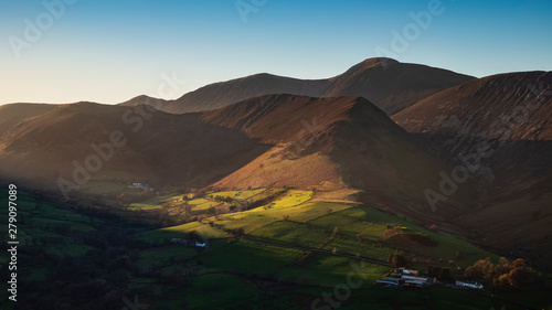 Beautiful Autumn Fall landscape image of sun beams lighting up small area of mountain side in Lake District whilst rest of area is in darkness with Robinson and Dale Head in background