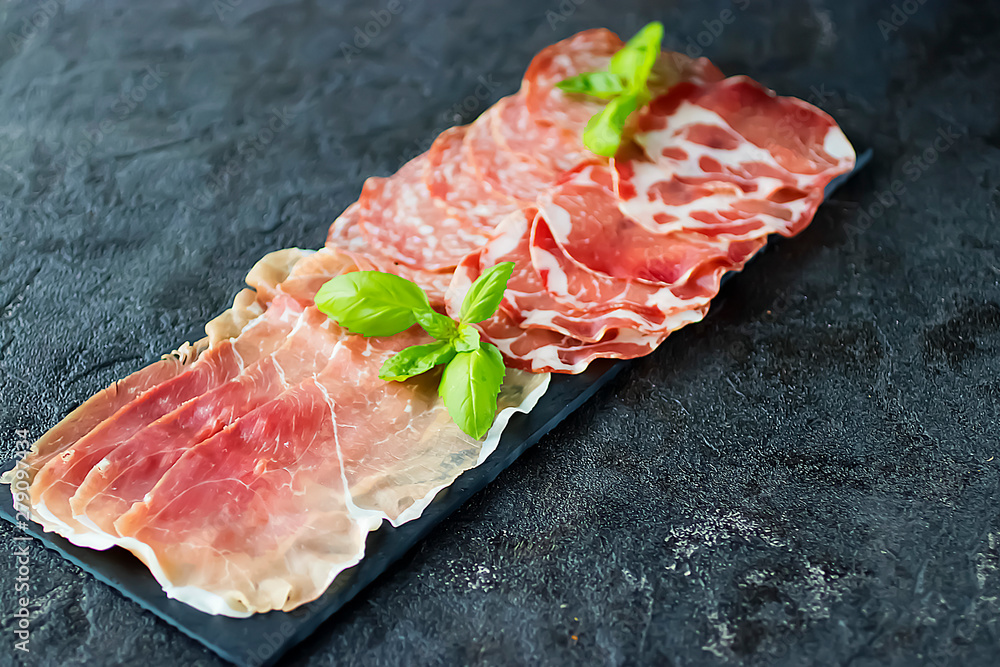 Italian meat snacks on a black slate board. Prosciutto Crudo, Milano Salami and Coppa Ham. Italian food. Italian meat snacks on a black slate board. Prosciutto Crudo, Milano Salami and Coppa Ham. Italian food.