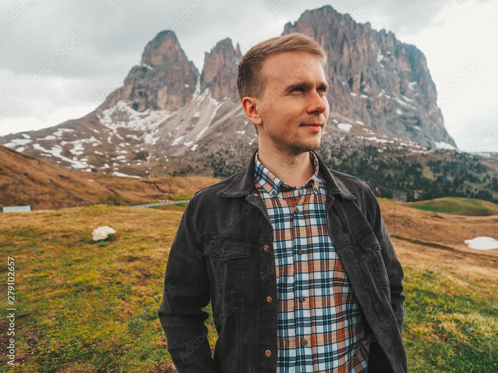 Naklejka premium A young man in a plaid shirt stands against the background of the Dolomites. Mountain summer landscape in the Dolomites in Northern Italy.