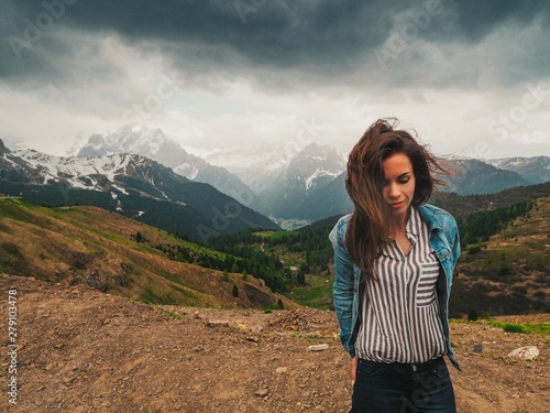 A brunette girl with long hair fluttering in the wind stands against the background of the Dolomite mountains. Mountain summer landscape in the Dolomites in Northern Italy.