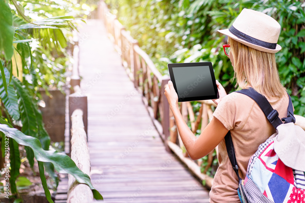 Fototapeta premium Travelling concept. Technology and adventure. Young woman using tablet computer in jungle.