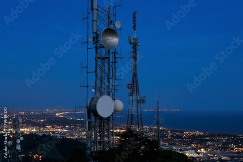 Telecommunications tower, antenna and satellite dish and coastline at night as background. Cellular station for smart city connect, aerial view.