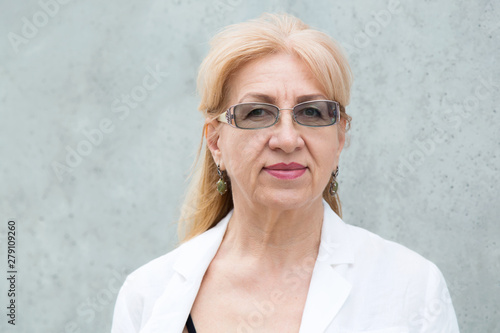 Close up portrait of happy mature woman in glasses, age 60 years against the gray wall. photo