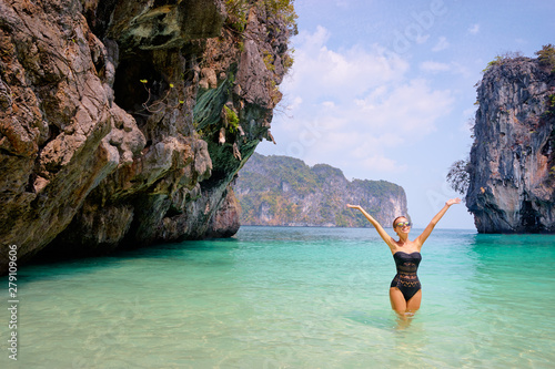 Vacation and happiness. Pretty young woman rising hands up standing on tropical beach with beautiful view in Thailand.