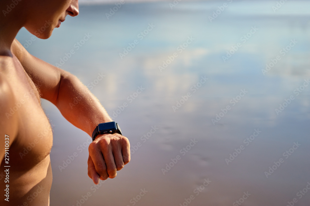Healthy lifestyle and technology. Young handsome strong man using smart watch tracker on the beach.