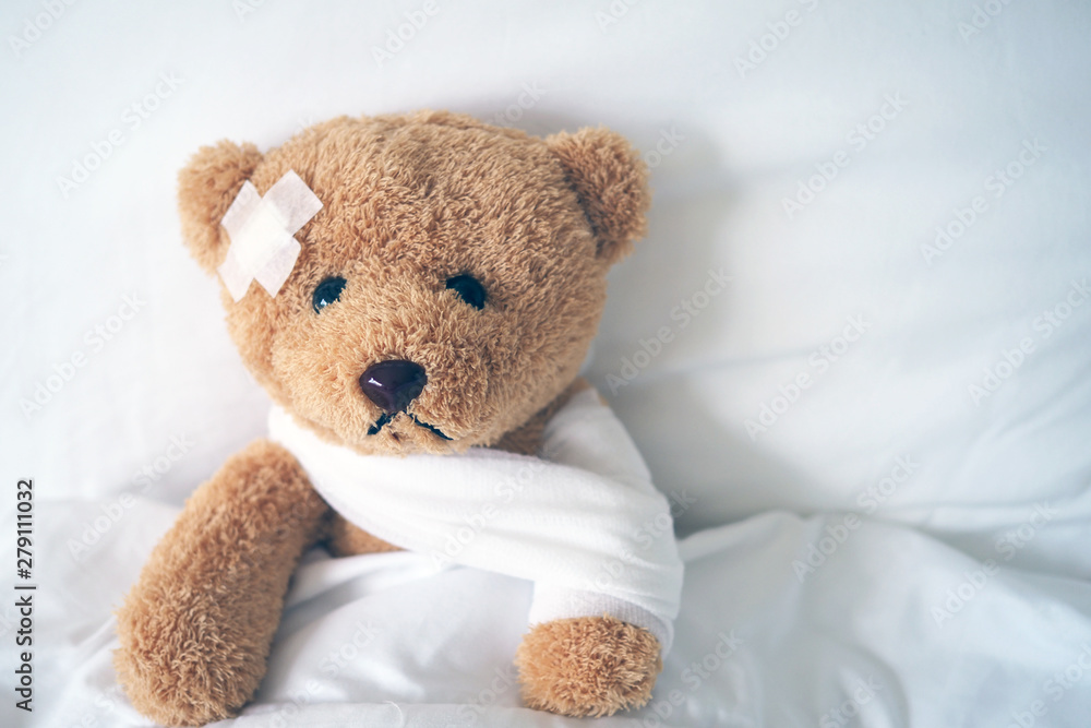 Teddy bear lying sick in bed With a headband and a cloth covered