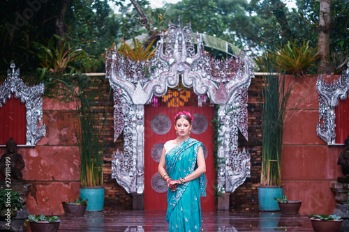 Beautiful young caucasian woman in traditional indian clothing with bridal makeup and jewelry. Bollywood dancer in Sari and henna on hands walking on temple garden.