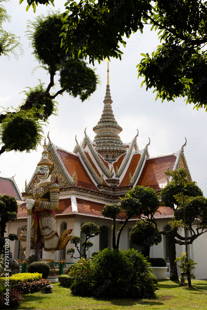 View of the roof of a Buddhist temple in Bangkok with white sky and green leaves