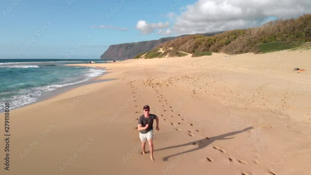 Version Two. Aerial Tracking Shot of Young Man Running on Golden Secluded Beach in Hawaii. Version Two. Aerial Tracking Shot of Young Man Running on Golden Secluded Beach in Hawaii.