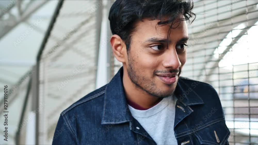 Fashionable guy in jean jacket raises his eyebrows and says something cute to a woman out of frame, laughs, and watches her walk past him Fashionable guy in jean jacket raises his eyebrows and says something cute to a woman out of frame, laughs, and watches her walk past him