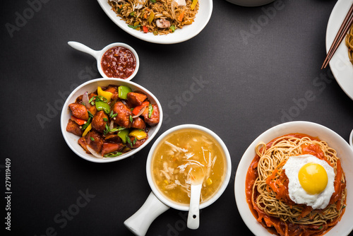 Assorted Indo chinese food in group includes non vegetarian or chicken Schezwan/Szechuan hakka noodles, fried rice, manchurian, egg american chop suey, soup with spoon and chop sticks, selective focus photo