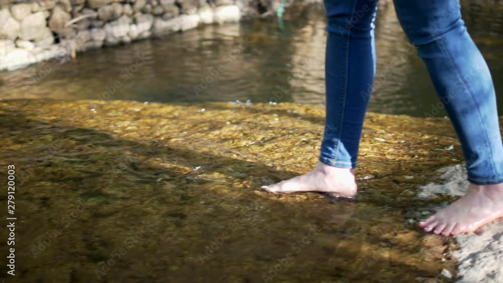 A woman dips her feet and toes in the water at a creek in the forest. A woman dips her feet and toes in the water at a creek in the forest.