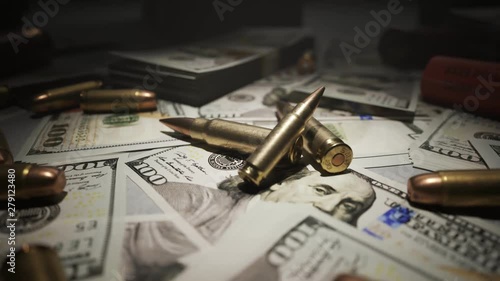 Small pile of ammo bullets on a table covered with countless dollar bills. 4KHD