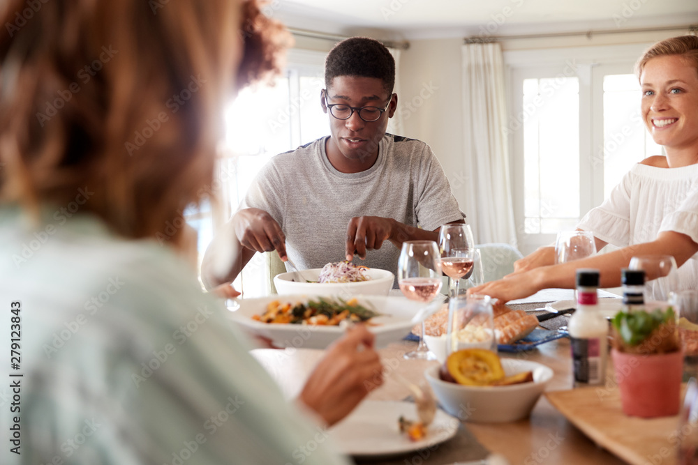 Millennial friends eating lunch together at a sitting at dinner table, close up Millennial friends eating lunch together at a sitting at dinner table, close up