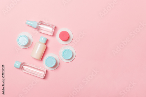 Set of travel size cosmetic bottles on pink background. Flat lay of cream jars. Top view of bodycare style concept