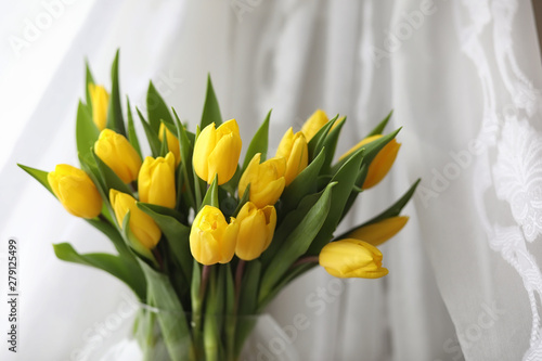 A bouquet of yellow tulips in a vase on the windowsill. A gift to a woman's day from yellow tulip flowers. Beautiful yellow flowers in a vase by window.