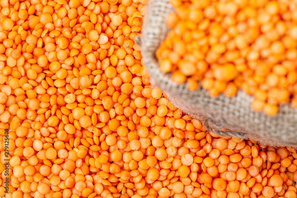 Red lentils in a sack cloth. Product photo of red lentils. Healthy lifestyle. Vegetarian and vegan diet. Spilled lens