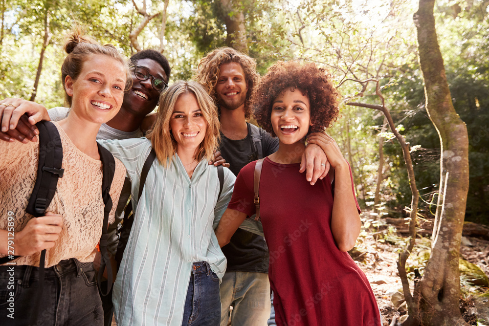 Five young adult friends hiking in a forest smiling to camera, three quarter length, close up