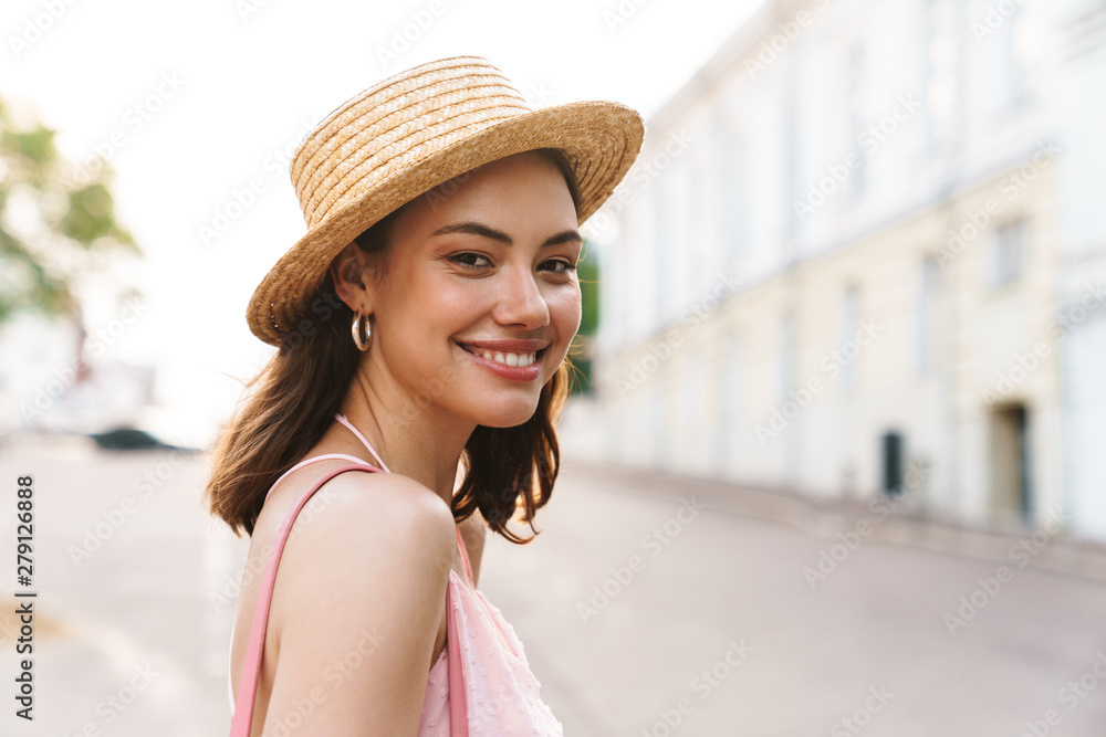 Photo closeup of lovely young woman wearing summer straw hat walking on city street