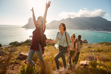 Young adult friends hiking single file uphill celebrate reaching a summit, full length, side view