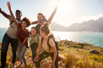 Millennial friends on a hiking trip celebrate reaching the summit and have fun posing for photos