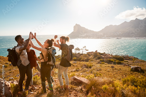 Young adult friends on a hike celebrate reaching a summit near the coast, full length, side view photo